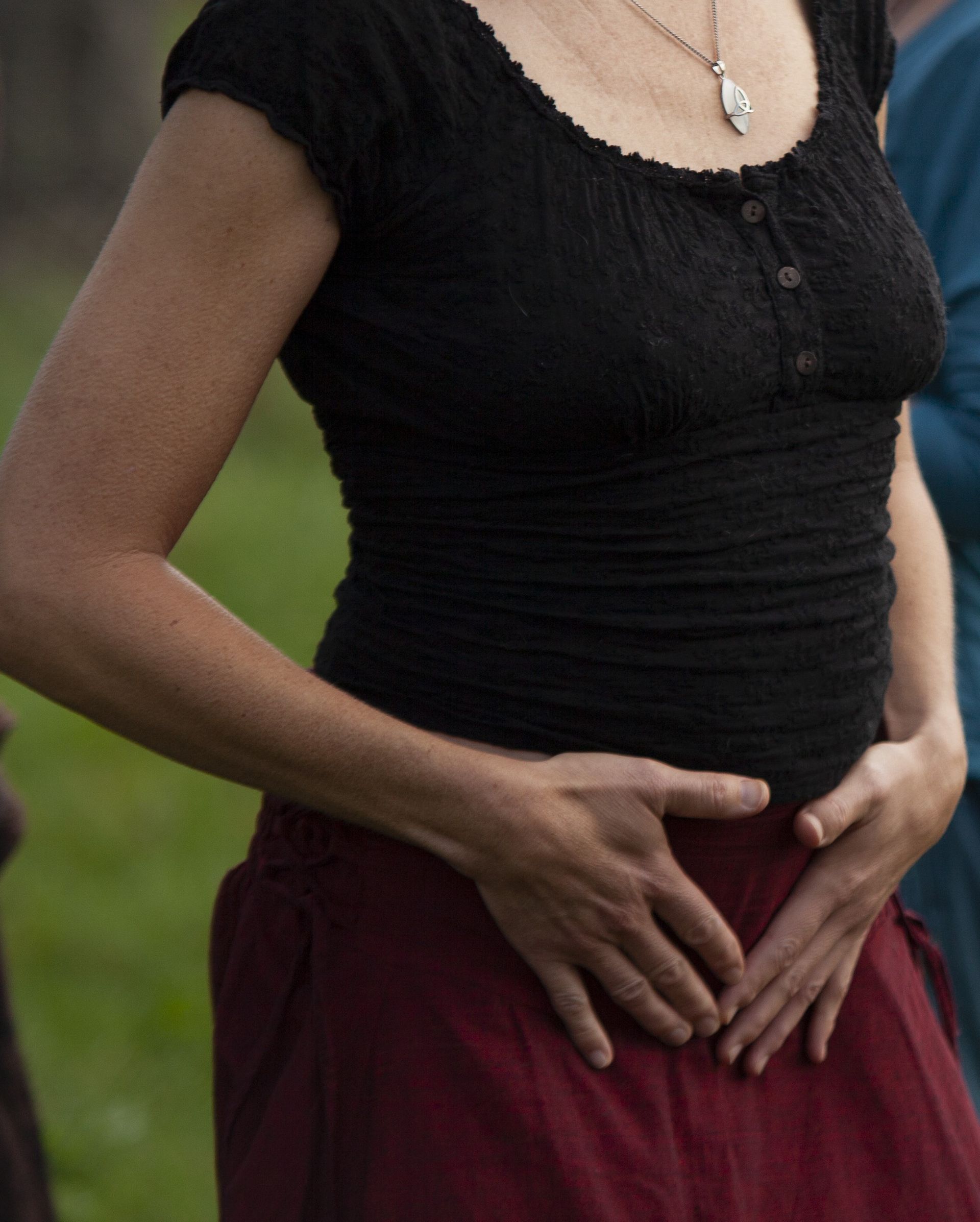 Een vrouw in een zwart topje en een rode rok houdt haar handen op haar buik