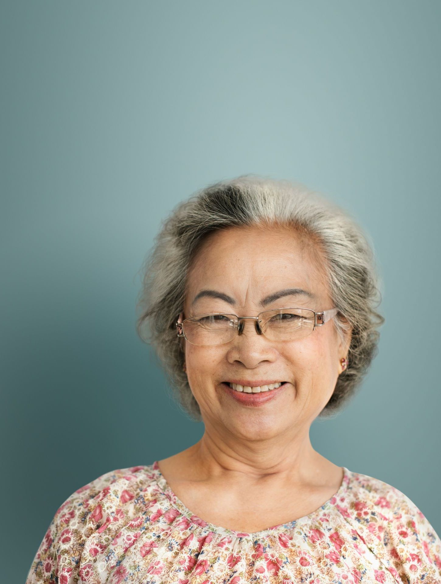 An elderly woman wearing glasses and a floral shirt is smiling.