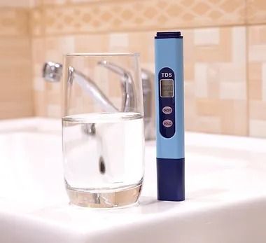 A glass of water next to a tds meter on a sink.