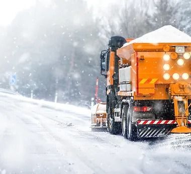 A snow plow is driving down a snow covered road.