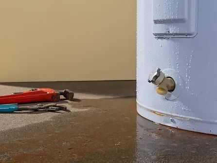 A water heater is sitting on the floor next to a pair of wrenches.