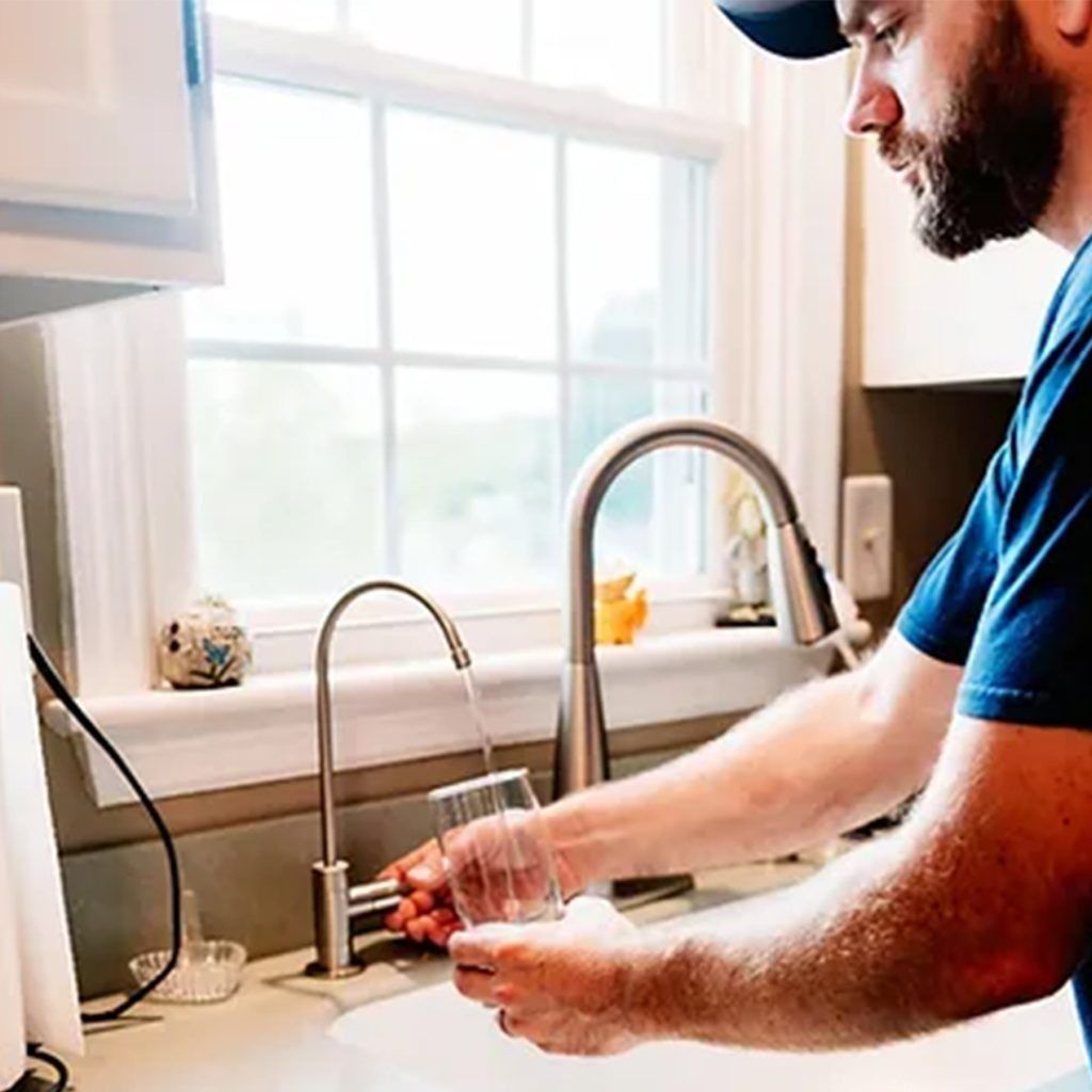 A man is pouring water into a glass in a kitchen sink.