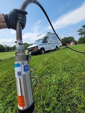 A person is holding a water pump in a field with a van in the background.