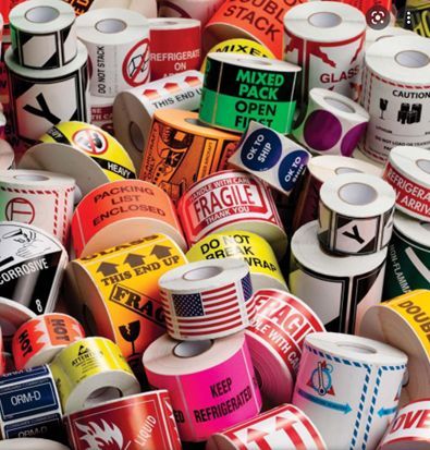 Surtido de rollos de etiquetas de envío y advertencia con diversos textos y símbolos, en múltiples colores.