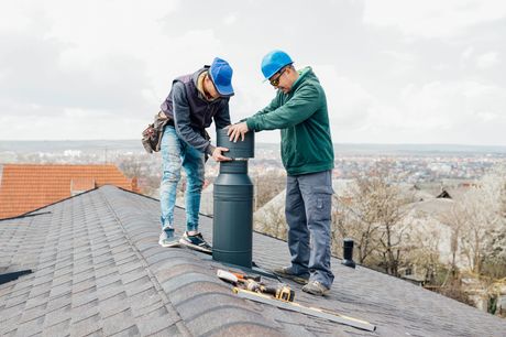 two professional masters Roofer construction workers repairing chimney on grey slate shingles roof of domestic house, sky background with copy space.

