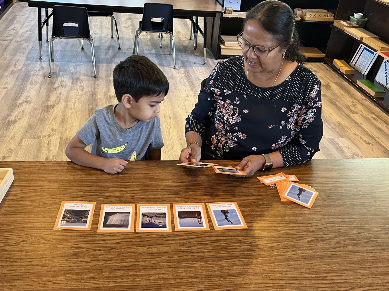 Adult and child looking at photo cards on a table in a classroom-like room