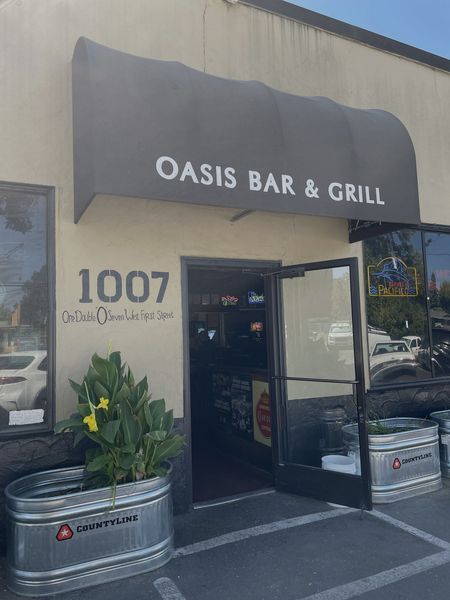 Oasis Bar & Grill storefront with awning. Door open, sign 