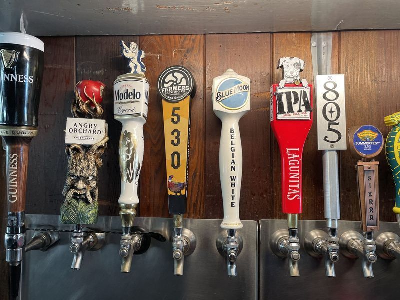 Beer taps with various logos lined up on a bar.