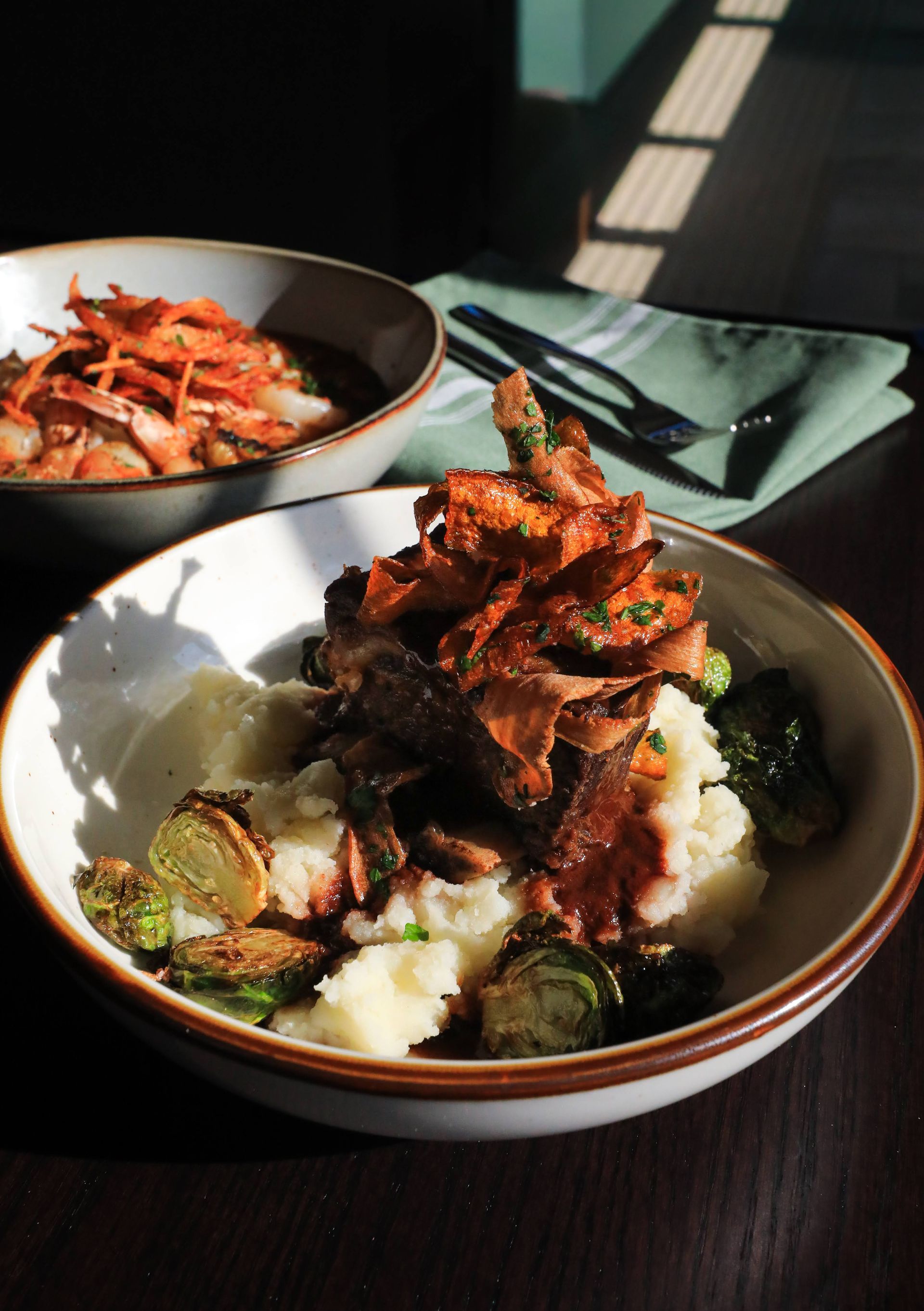 Two bowls of food: braised meat with mashed potatoes and Brussels sprouts, and shrimp with carrots.