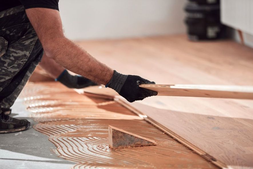 Person installing hardwood flooring, applying adhesive.