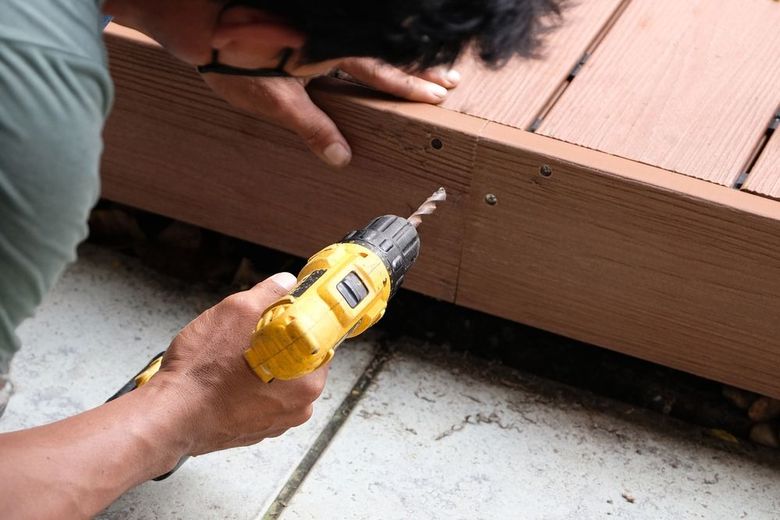 Person using a yellow drill to screw into a brown wooden deck.