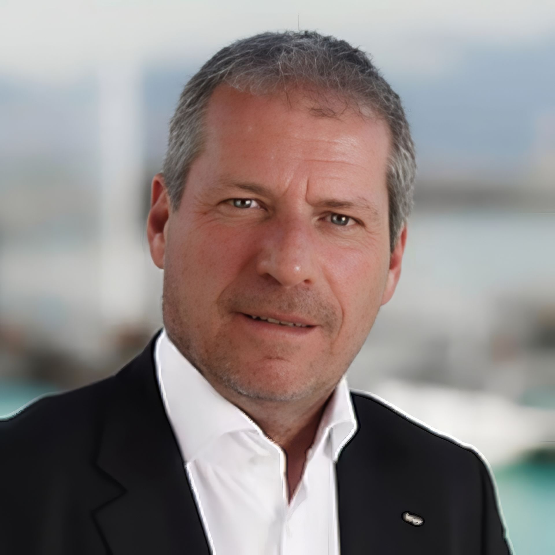 Un homme en costume et chemise blanche sourit à la caméra.