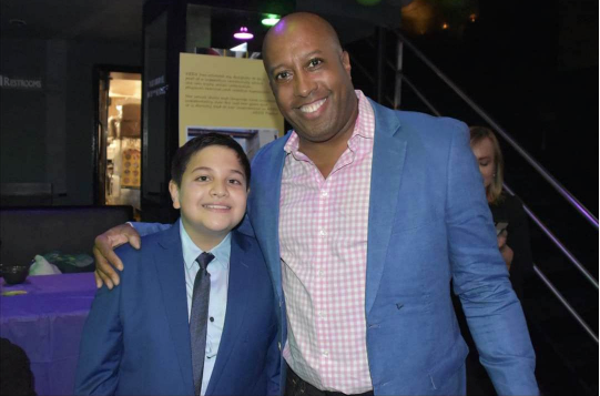 Keen athlete, Enrique, stands on the left next to KEEN Board Director Joseph Chapman to the right. They are both smiling at the camera and wearing suits at the 2021 KEENFest gala.