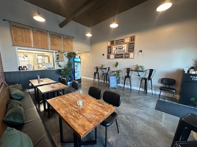 Restaurant interior: tables, chairs, menu boards, brick, and gray walls. Natural wood tables and leather benches.