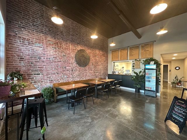 Interior of a cafe with brick wall, tables, chairs, and concrete floor. Overhead lights illuminate the space.