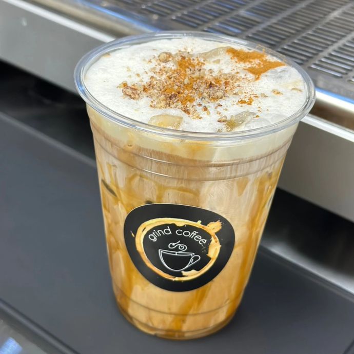 Iced coffee drink with caramel drizzle, topped with cream and cinnamon in a plastic cup.