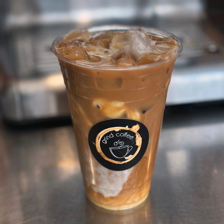 Iced coffee in a clear plastic cup, layered with cream, coffee, and ice. Black logo on the cup.