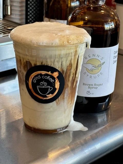 Iced coffee drink with foam overflowing the cup; next to a bottle of brown sugar syrup.