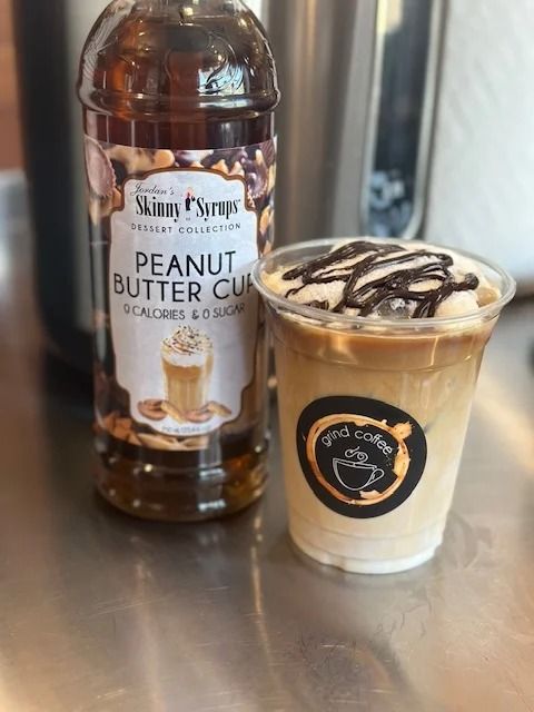 Bottle of peanut butter cup syrup next to an iced coffee drink with chocolate drizzle.
