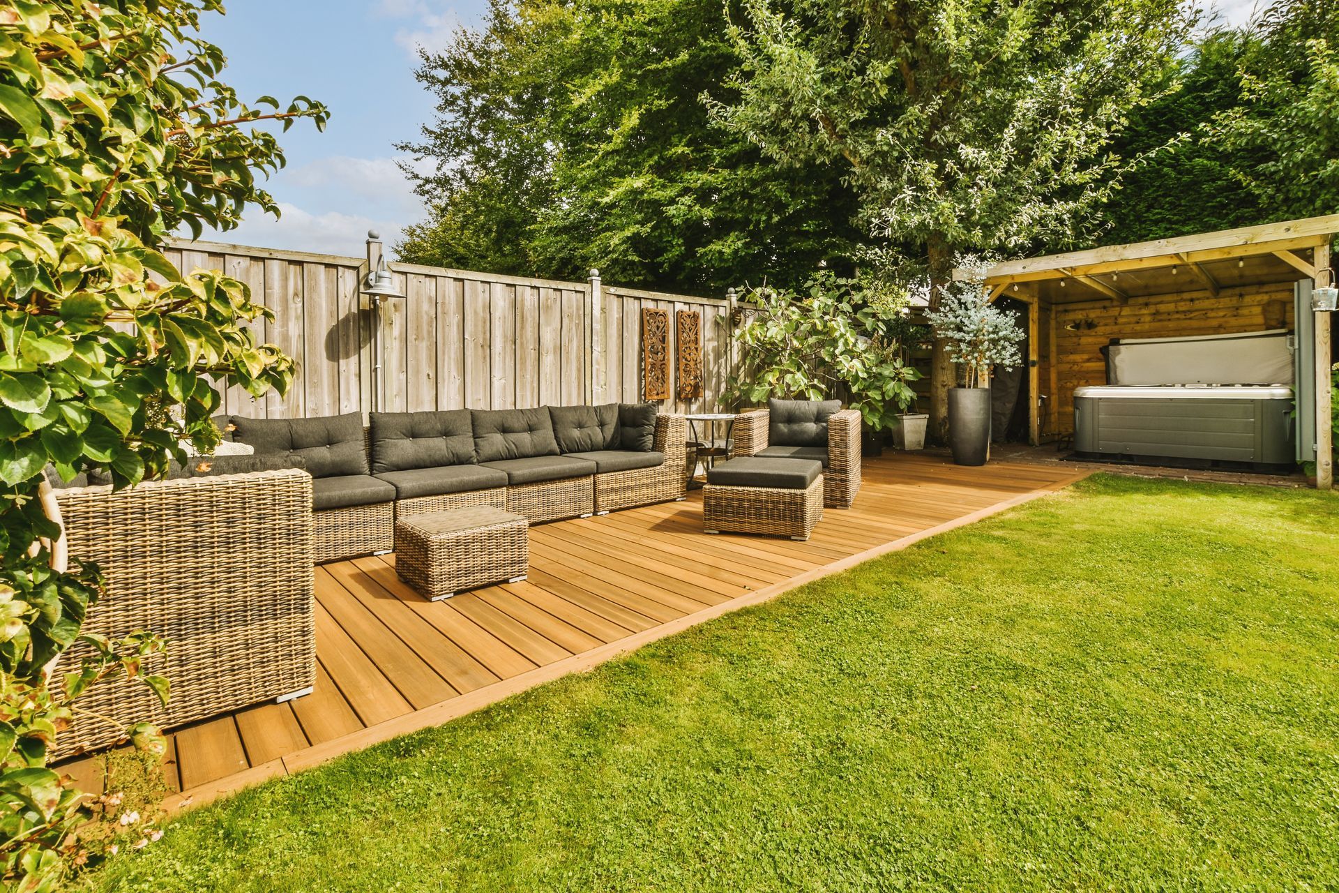 Outdoor lounge area with wicker furniture on wooden deck next to a hot tub.