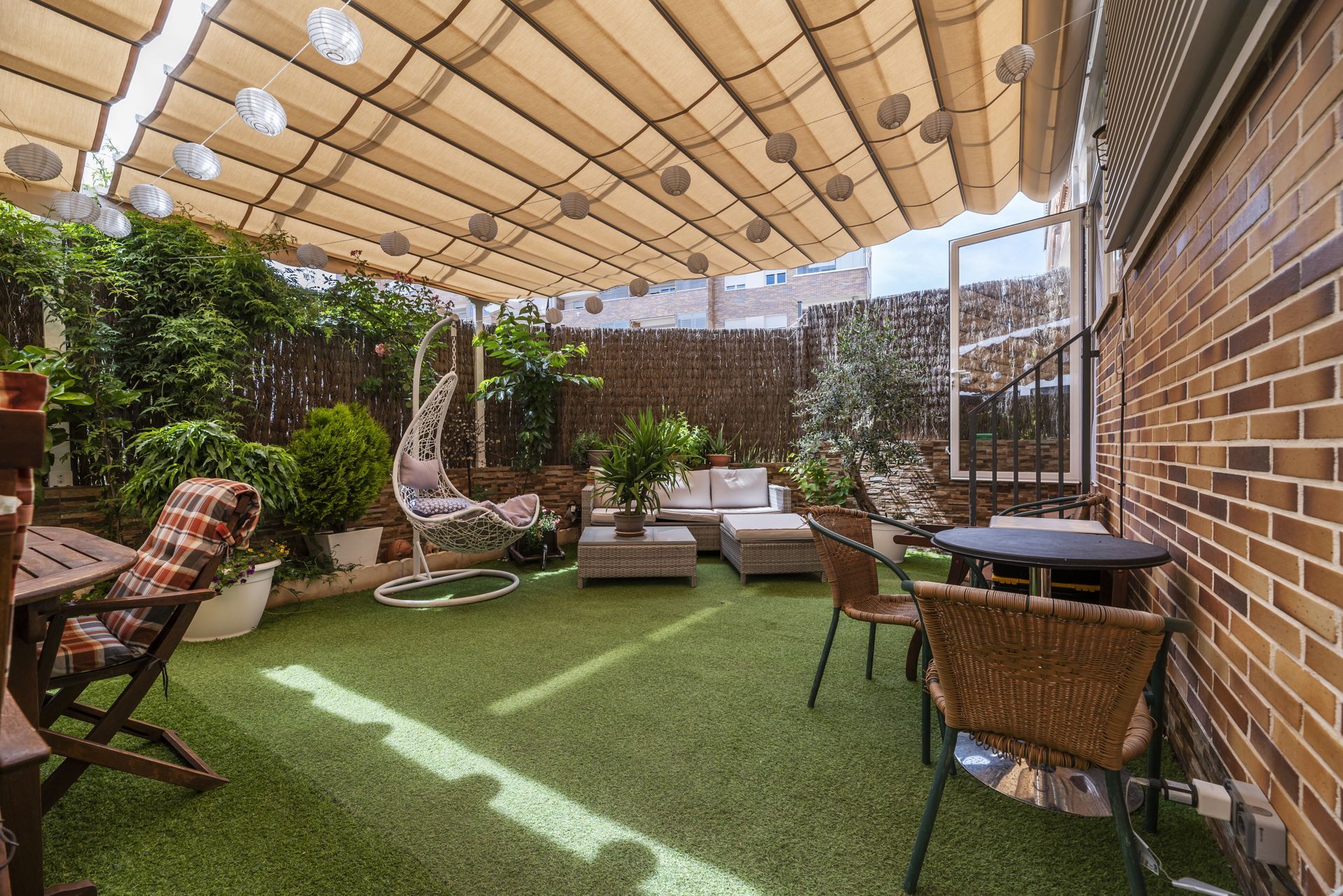 A backyard patio with artificial grass, lounge furniture, plants, and a retractable awning.
