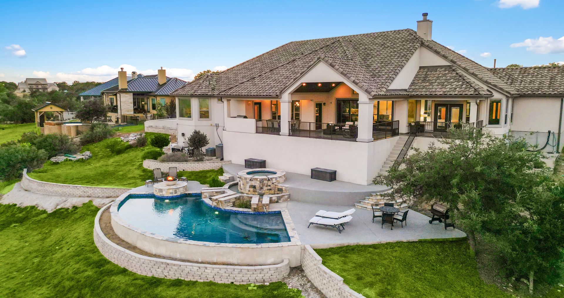 Luxurious house with pool and patio on a hill, overlooking green landscape.