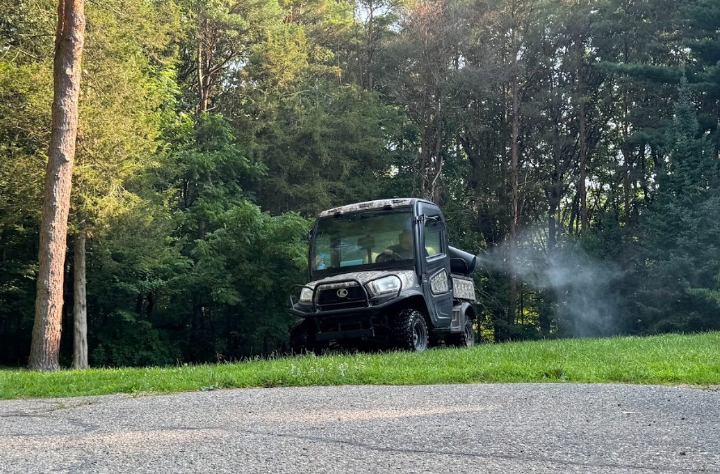 Utility vehicle spraying a mist in a grassy area near trees.