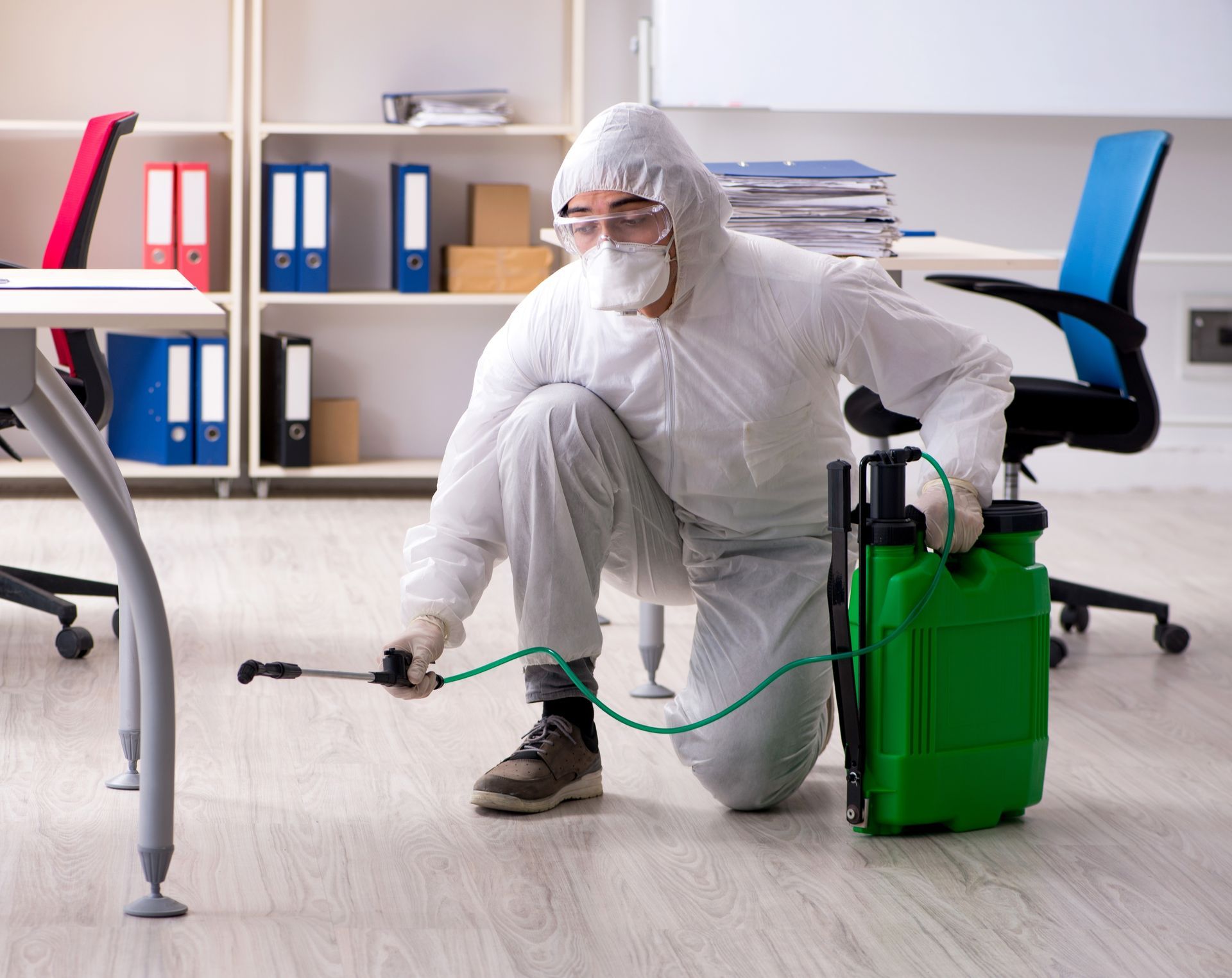 Person in hazmat suit spraying insecticide in an office.