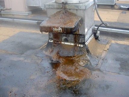 Rooftop HVAC unit with significant rust and leakage staining the black tar roof.