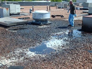 Man on a gravel roof with standing water, near HVAC units and a vent.