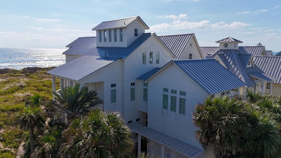 A large white house with a blue roof is sitting on top of a hill next to the ocean.