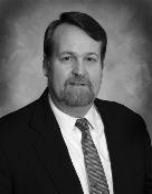 A middle-aged man with a beard and dark suit, looking directly at the camera.