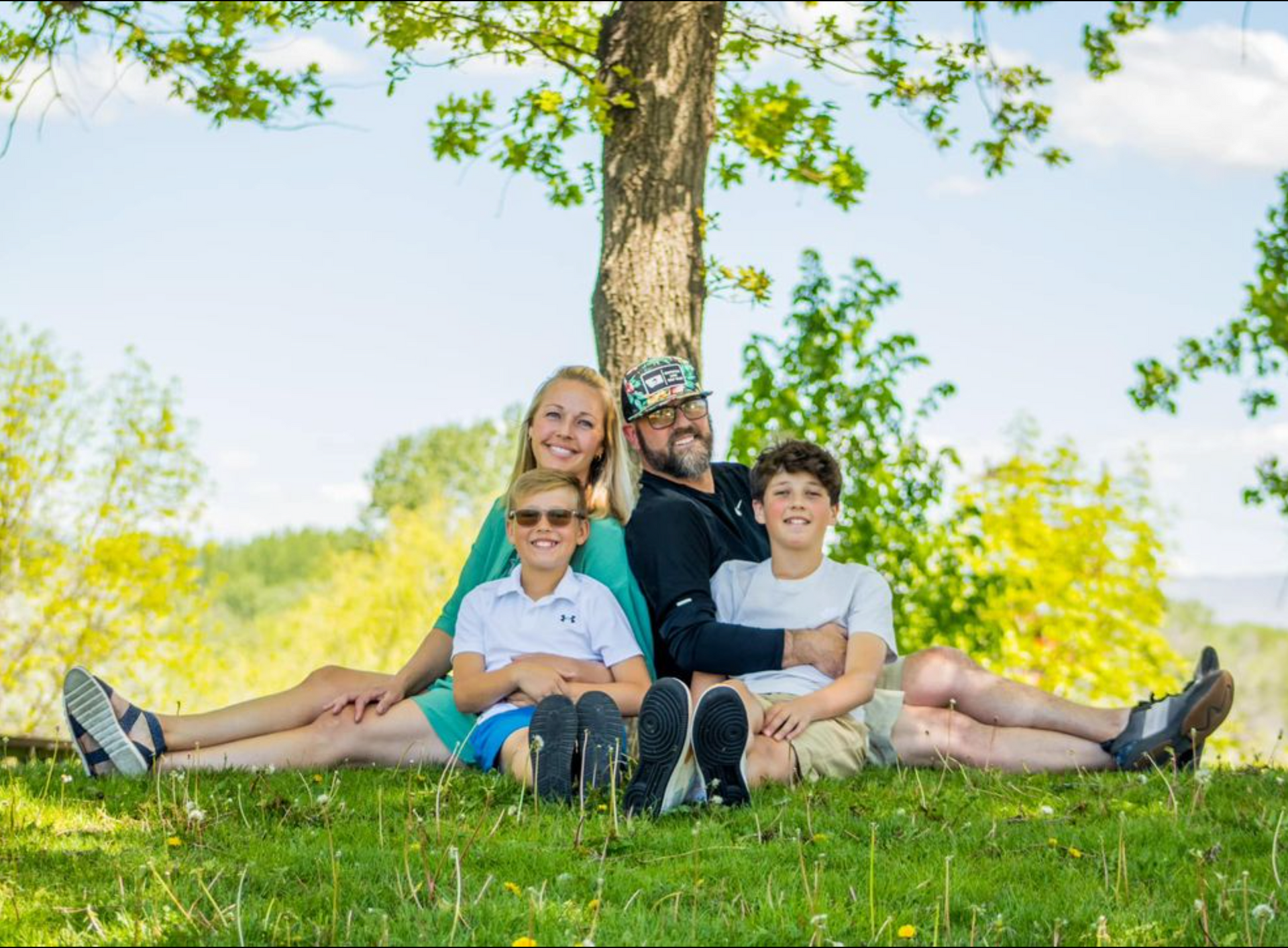 A family is sitting under a tree in the grass.
