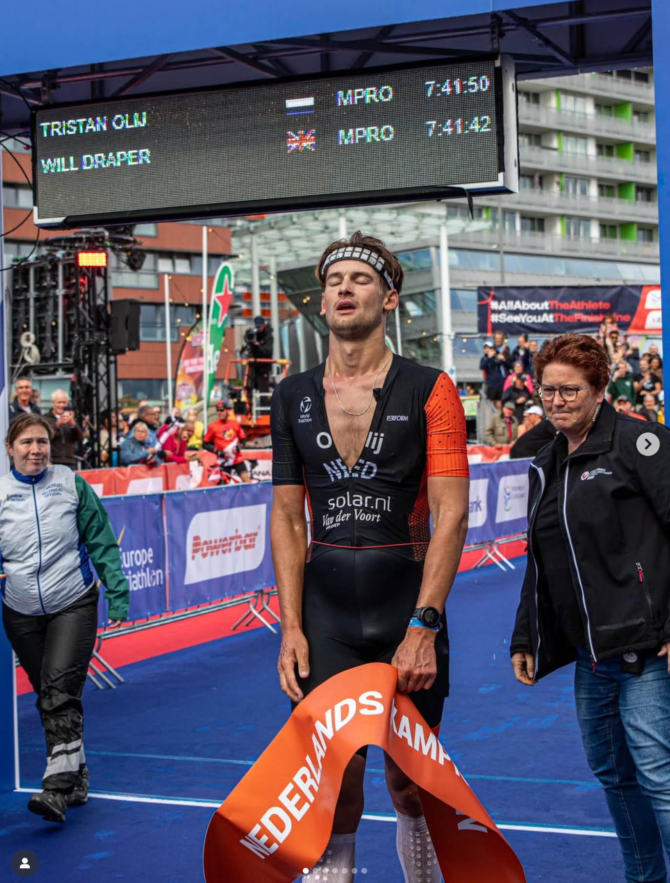 Triathlete on a white Trek bike riding on a road near grassy dunes on a sunny day. Tailwind wheels