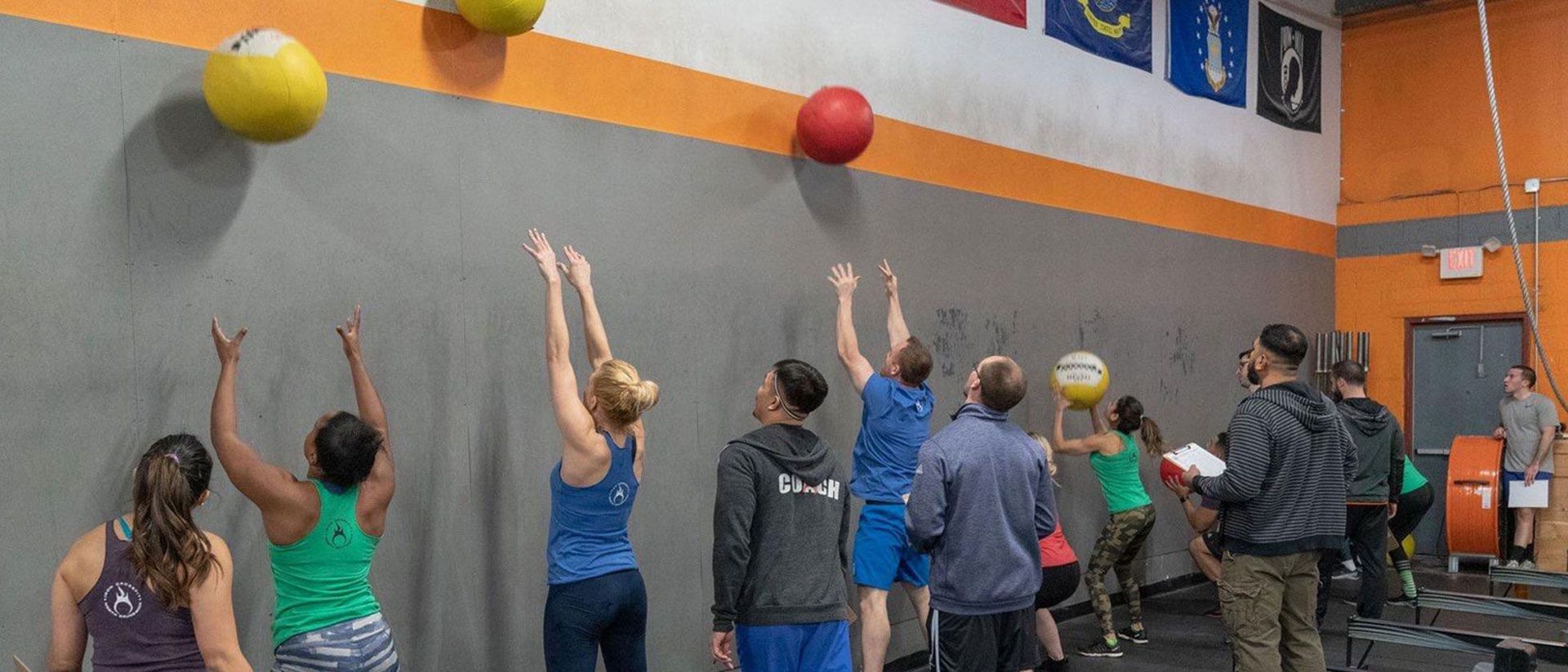 A group of people are throwing medicine balls at a wall in a gym.