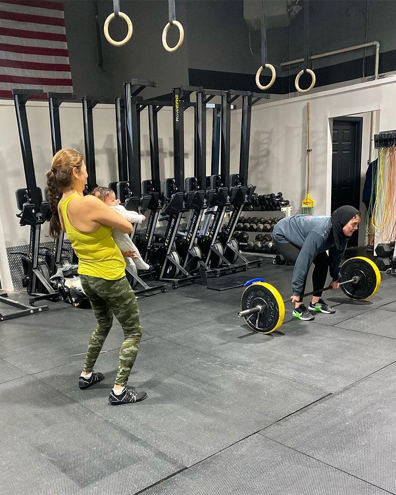 A woman is standing next to a man lifting a barbell in a gym.
