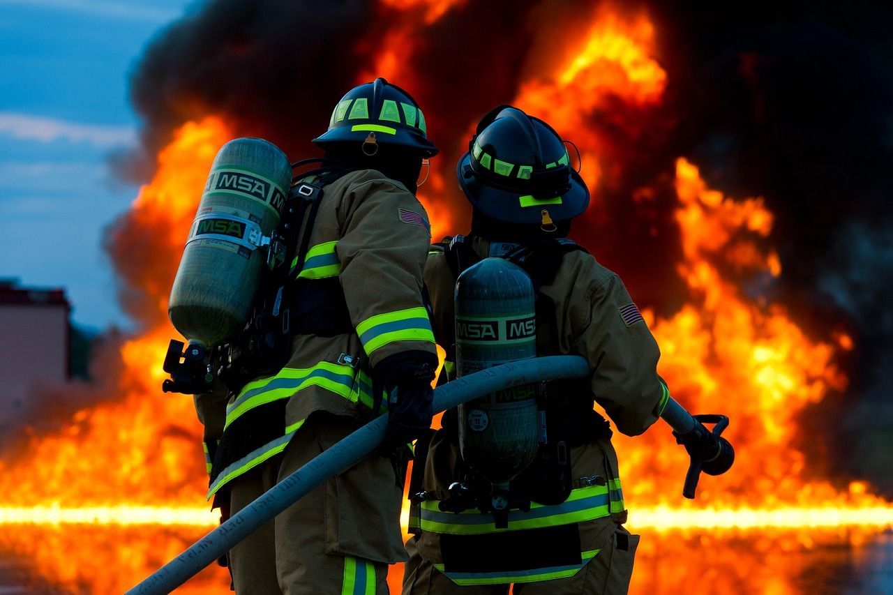 Two firefighters are standing in front of a large fire.