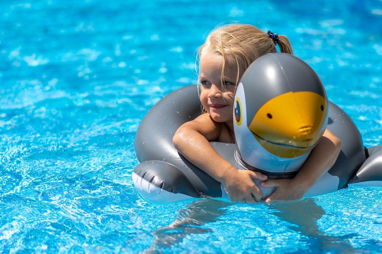 A little girl is floating on an inflatable penguin in a swimming pool.