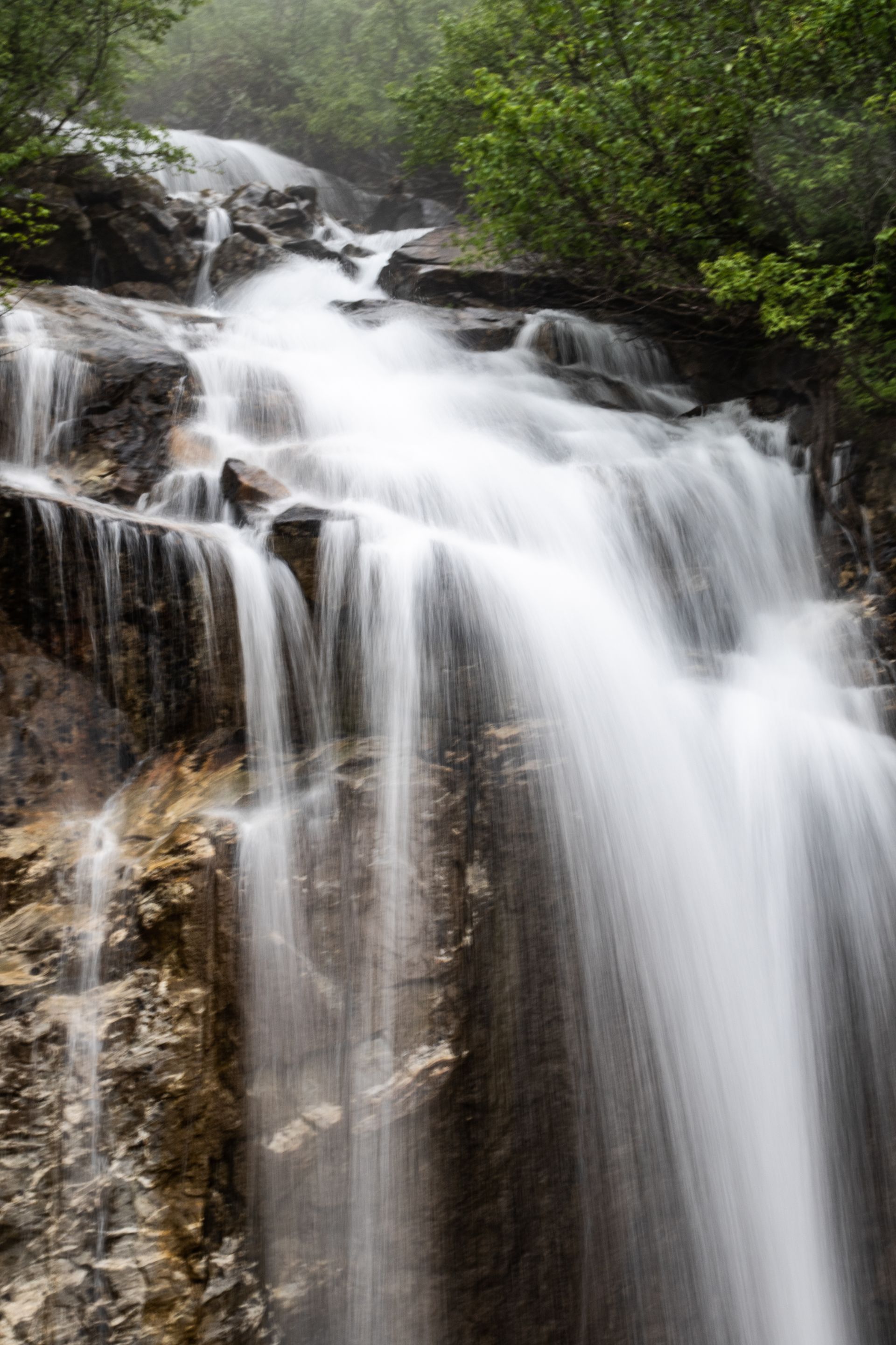Waterfall cascading over rocky cliffs, surrounded by green foliage.