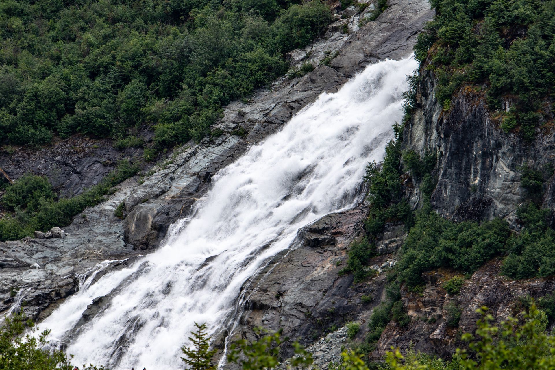 Waterfall cascading down a rocky mountainside, surrounded by lush green trees.