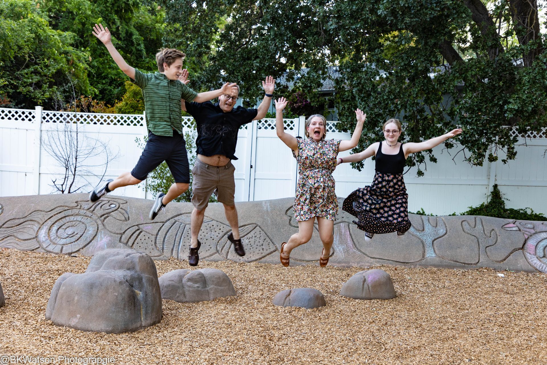Four people jumping in the air in a park with raised arms and happy expressions.