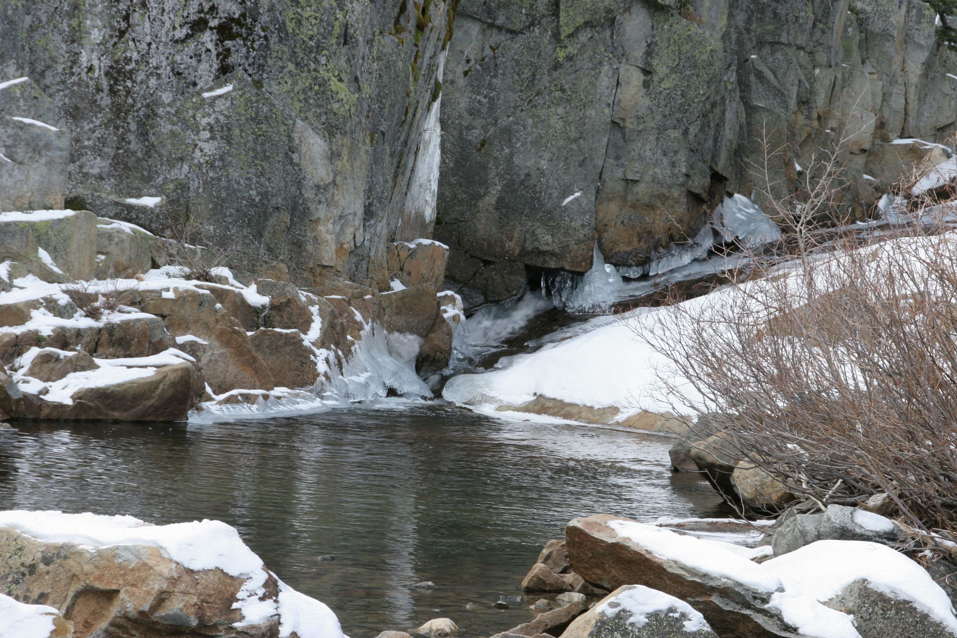 Snowy landscape with a small pond and waterfall flowing from rocky cliffs.