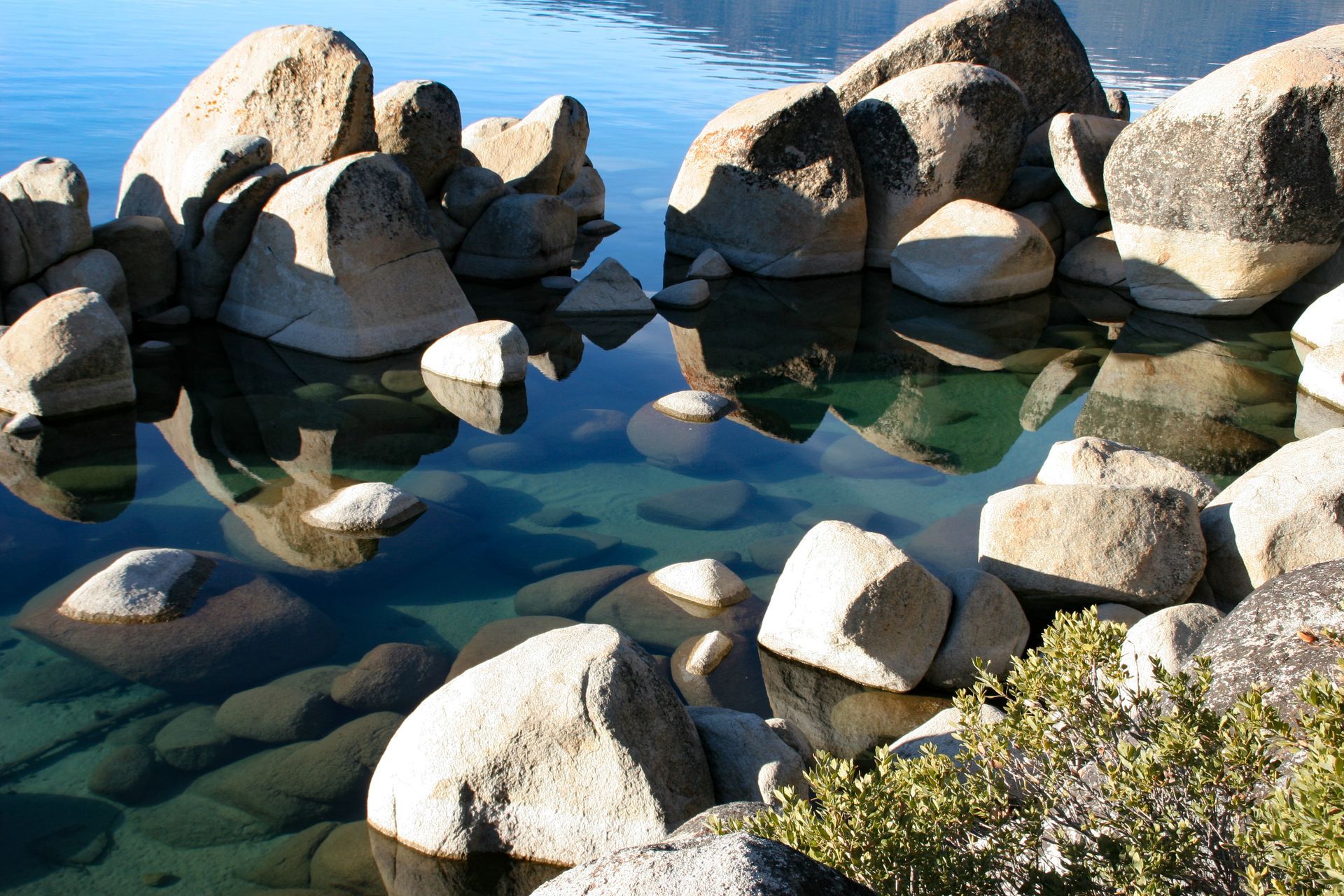 Large, light-colored boulders in shallow, clear water, reflecting the sky.