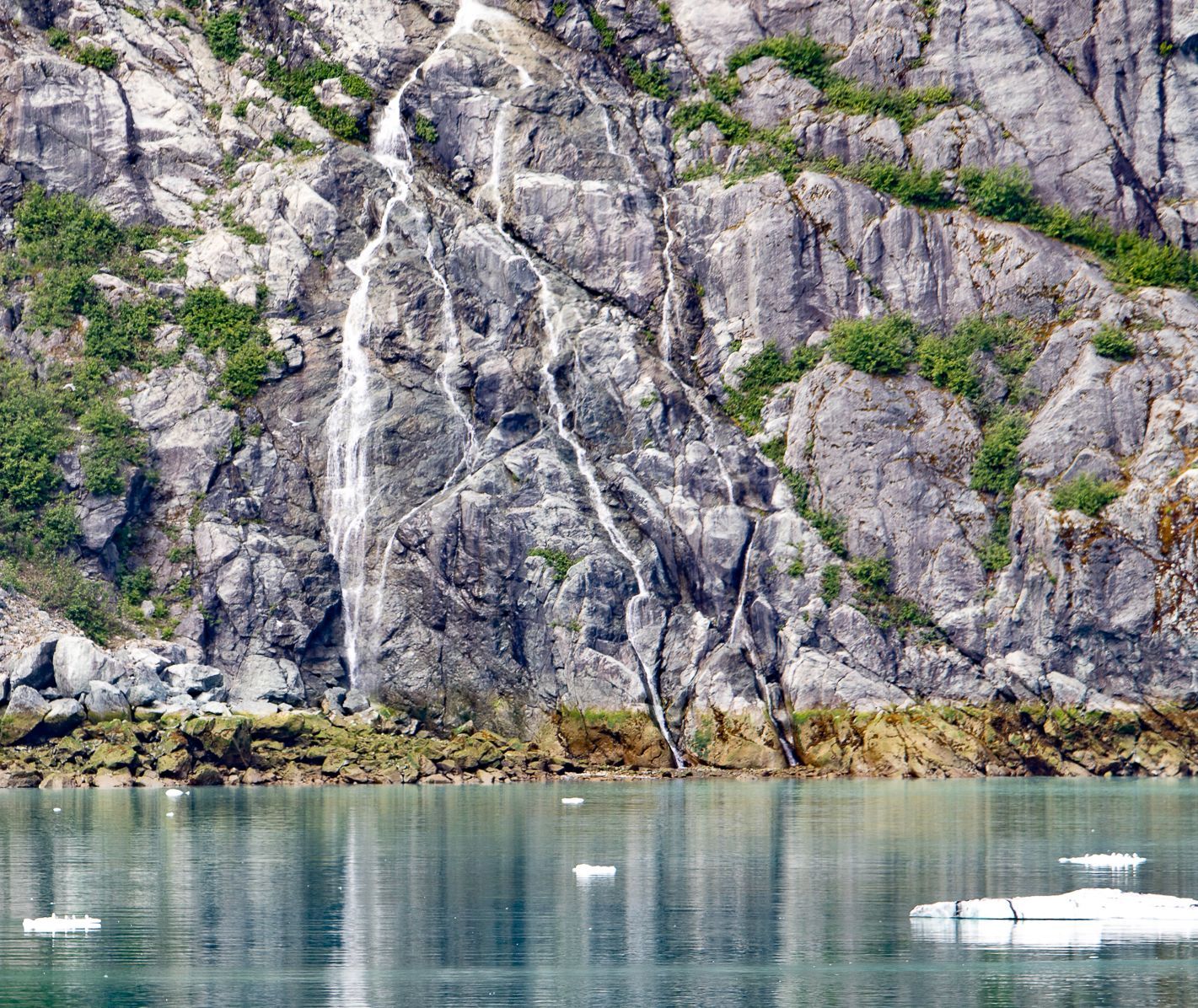 Rocky mountainside with a waterfall cascading into a glacial bay, small ice floes scattered.