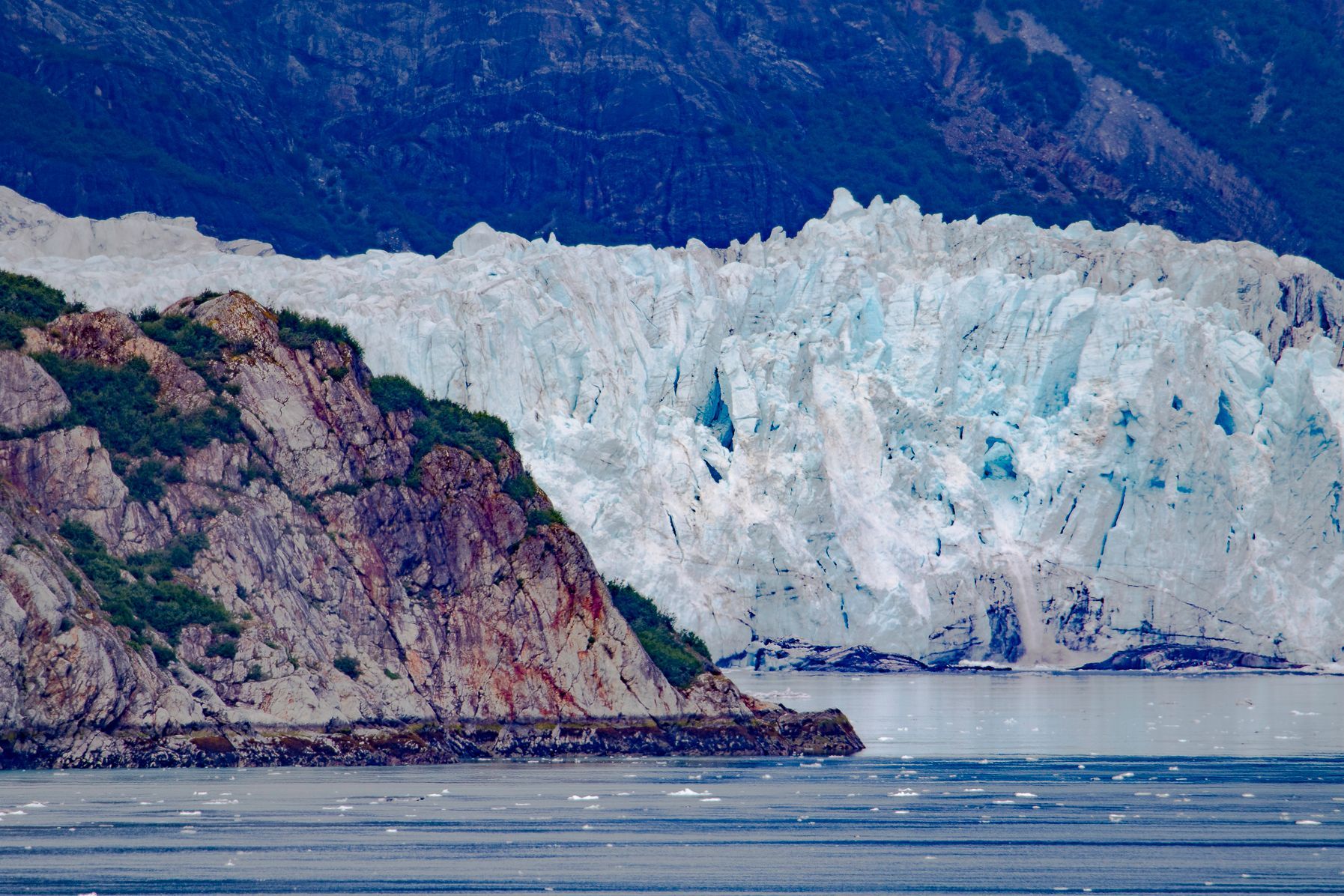 Glacier meets rocky shoreline; icy blue glacier contrasts with brown rock and sea.