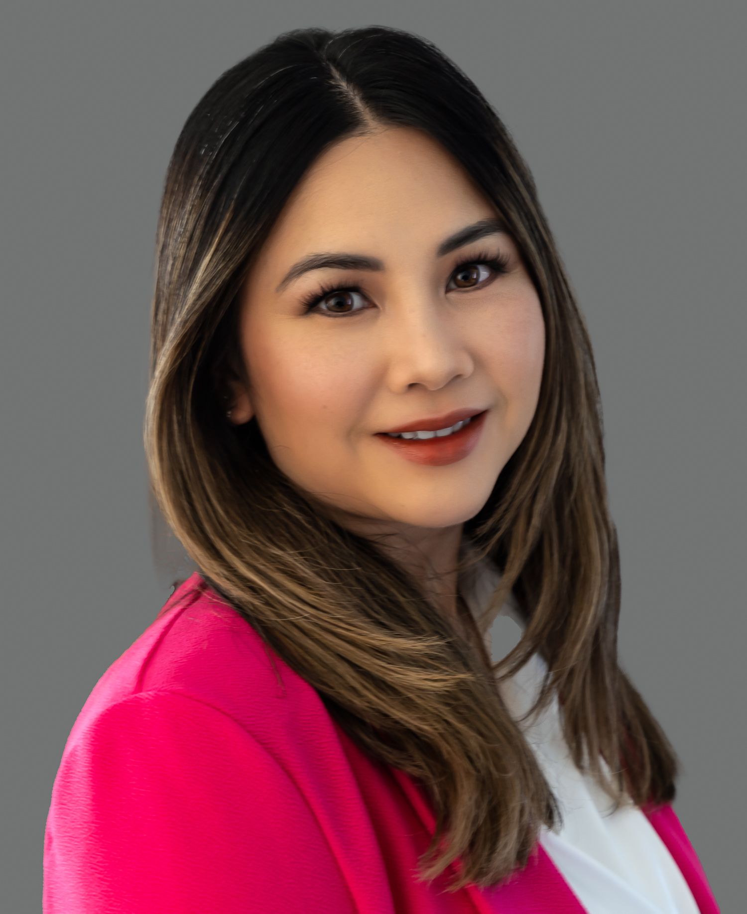Woman with brown hair in a pink blazer smiles at the camera against a gray background.