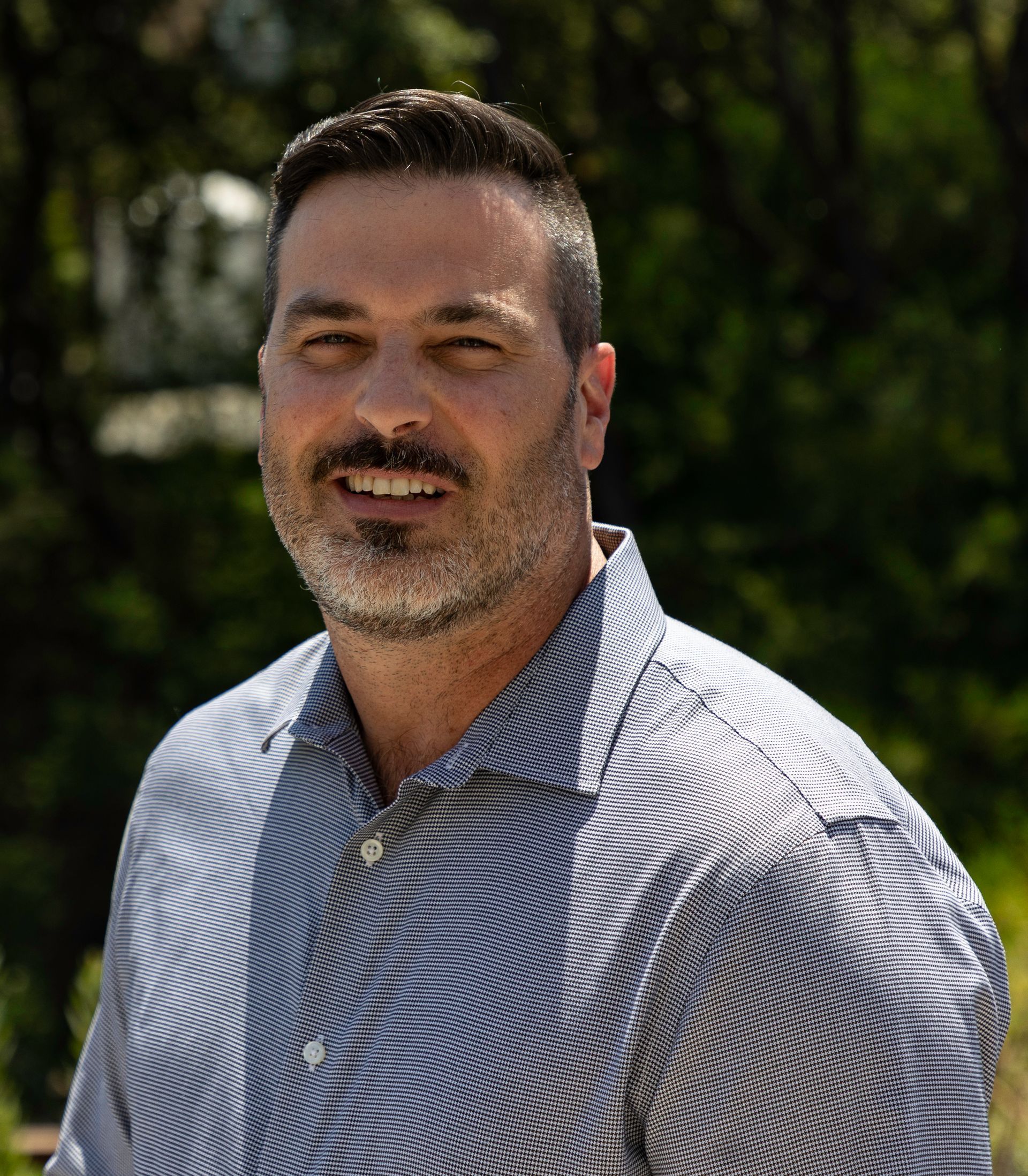 Man smiling, wearing a striped blue shirt, outdoors.