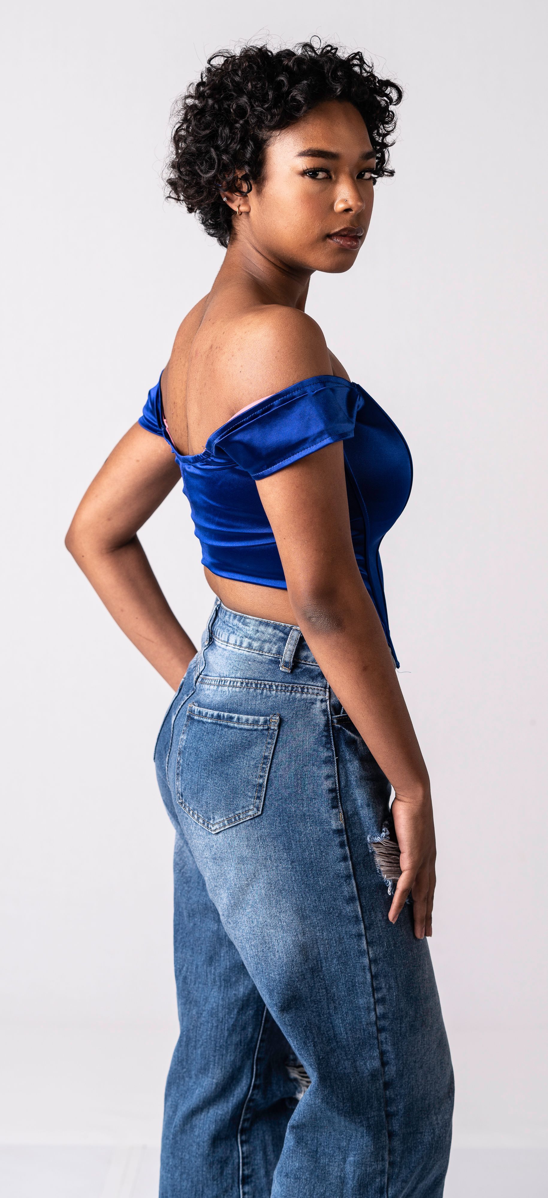 Woman in blue off-shoulder top and acid wash jeans, posing against a white background.