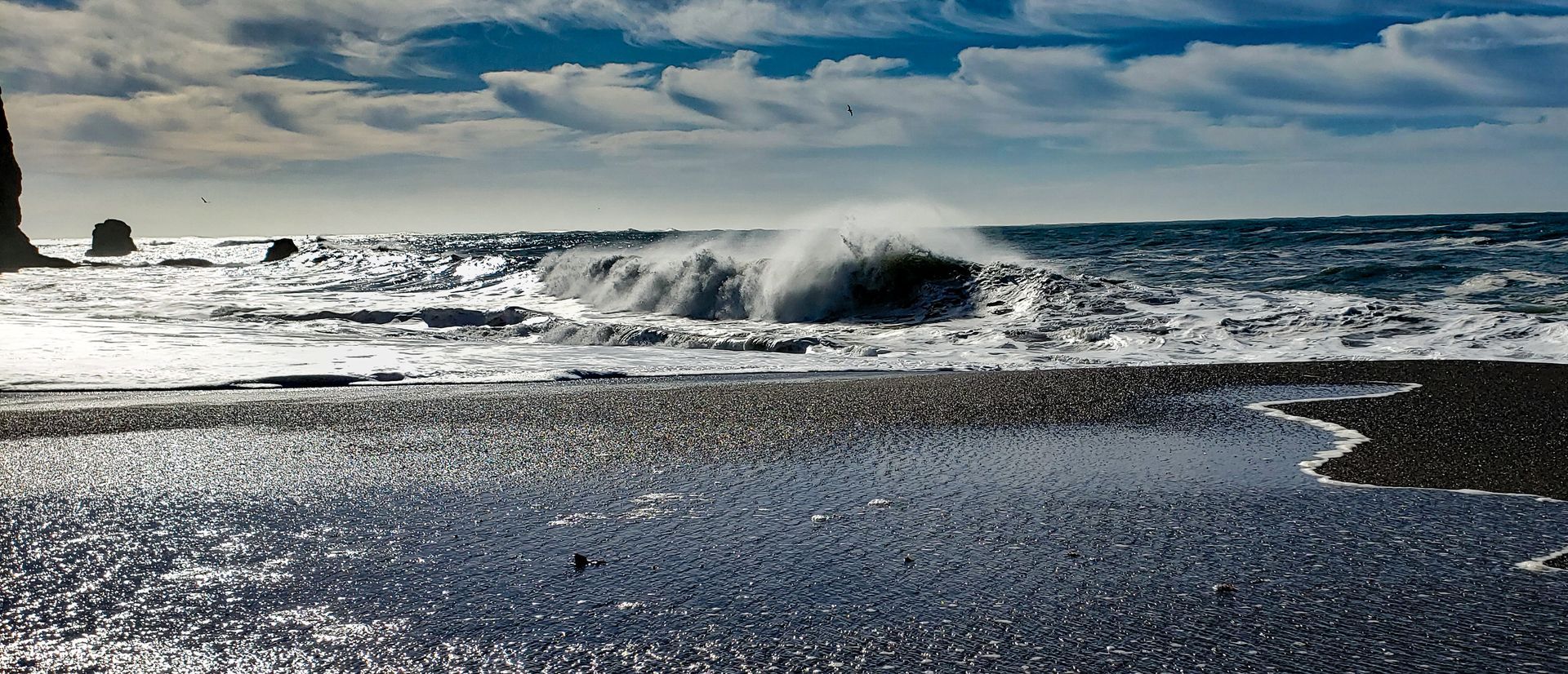 Waves crashing on a pebble beach under a cloudy sky.
