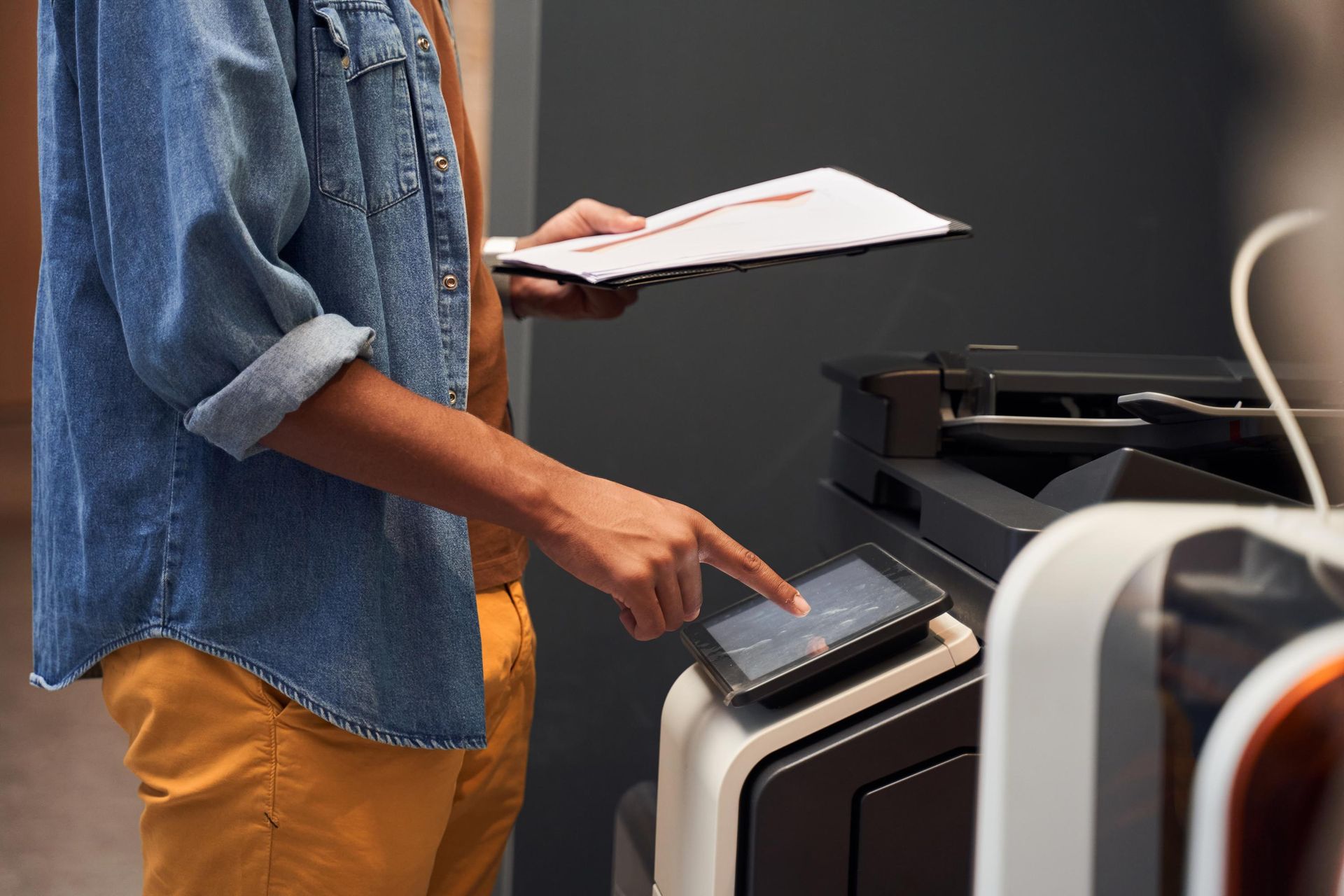 Person in denim shirt, yellow pants using a printer.